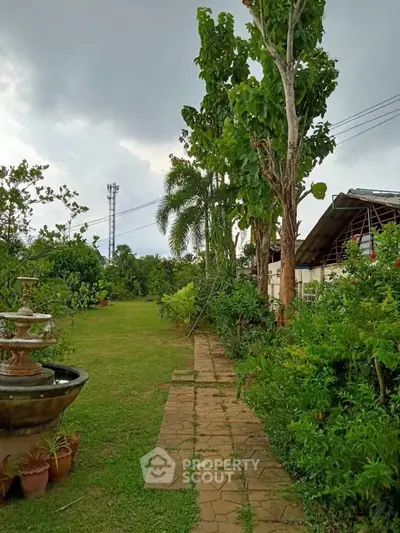 Lush garden with stone pathway and fountain in serene residential setting.