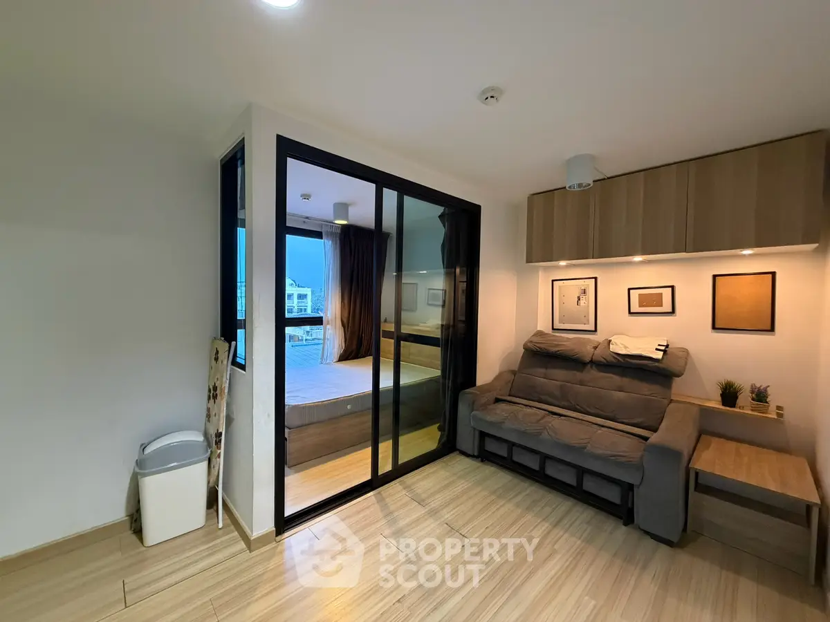 Modern living room with cozy sofa and glass partition leading to bedroom, featuring stylish decor and wooden flooring.