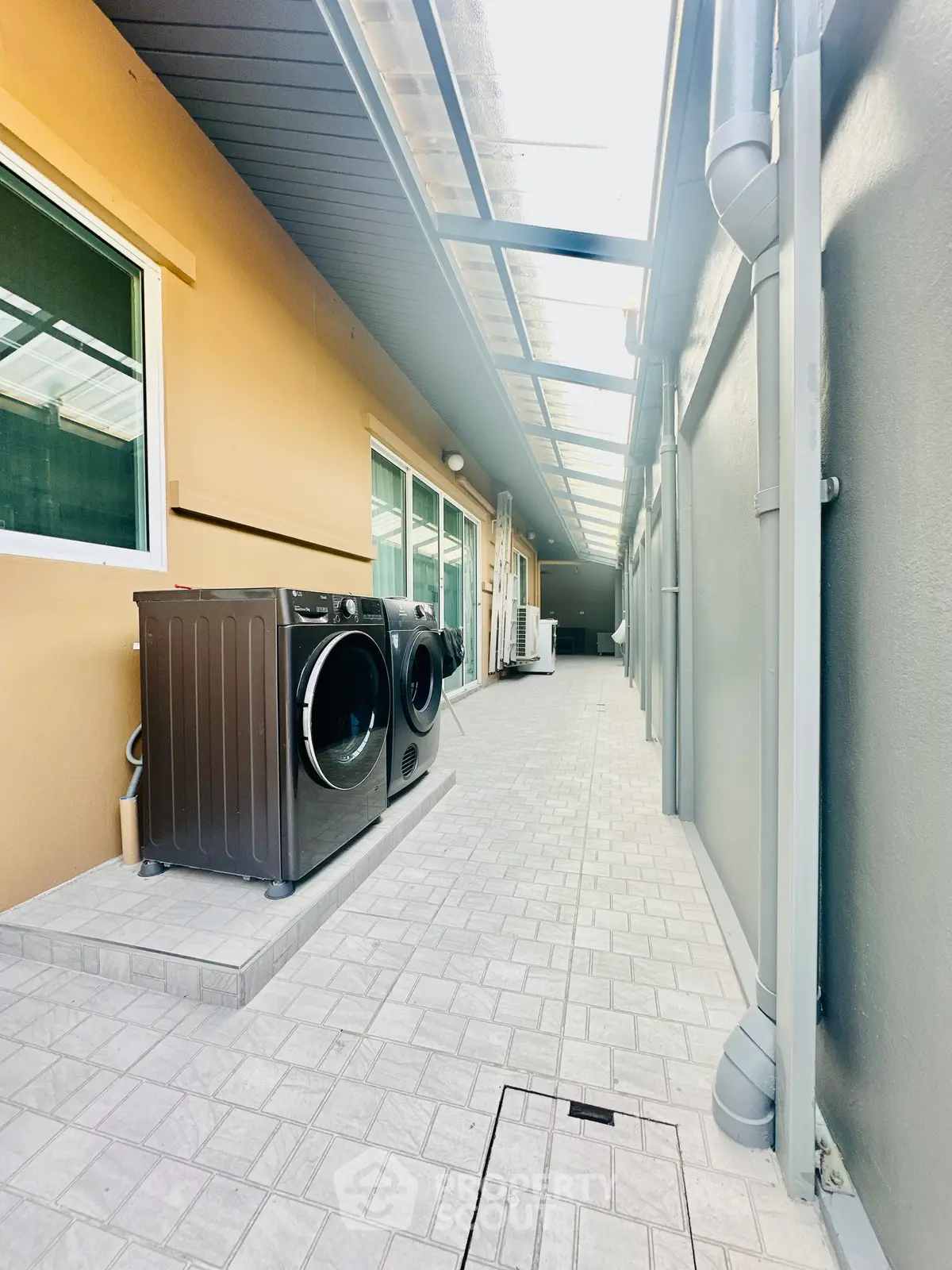Spacious outdoor laundry area with modern washing machine and covered walkway.