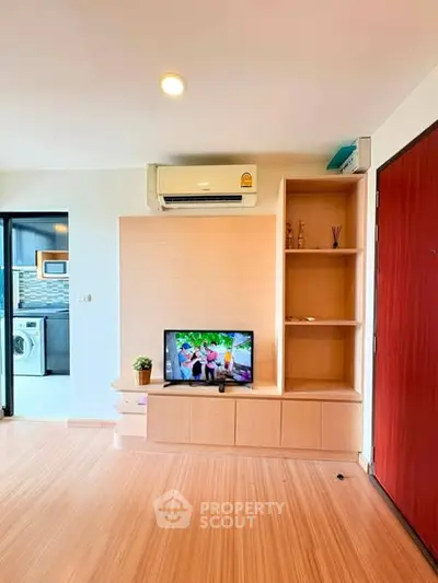 Modern living room with built-in shelves and air conditioning, adjacent to a kitchen with washing machine.