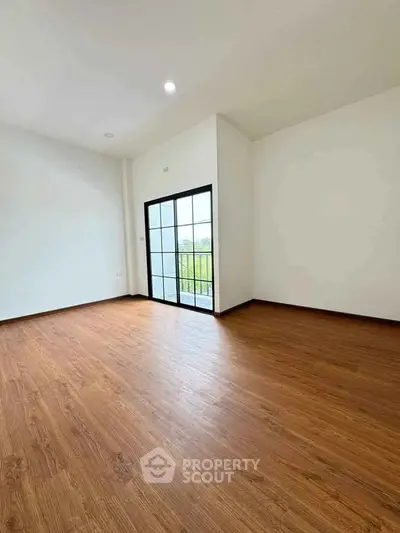 Spacious empty room with wooden flooring and large window offering natural light.
