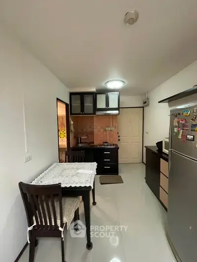 Cozy kitchen with dining area in modern apartment, featuring sleek cabinets and stainless steel fridge.