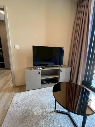Modern living room with sleek TV stand and glass coffee table, featuring floor-to-ceiling windows and elegant curtains.