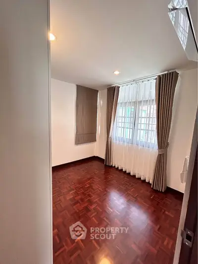 Spacious bedroom with wooden flooring and large window with curtains, perfect for cozy living.