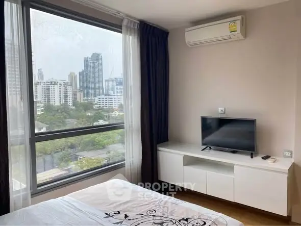 Modern bedroom with city view, featuring large window, air conditioning, and sleek TV setup.