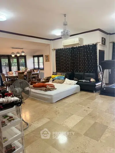 Spacious living room with elegant chandelier and marble flooring, featuring a cozy seating area and dining space.