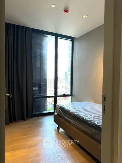 Modern bedroom with large window and city view, featuring sleek design and natural light.