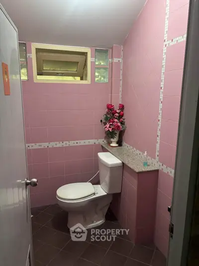 Charming pink-tiled bathroom with modern fixtures and decorative floral arrangement.
