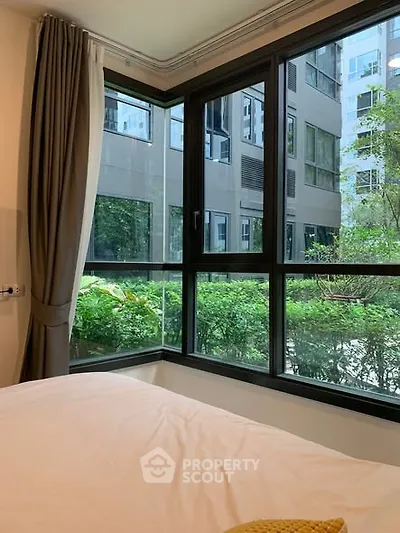 Bright bedroom with large windows offering a lush garden view in a modern apartment.