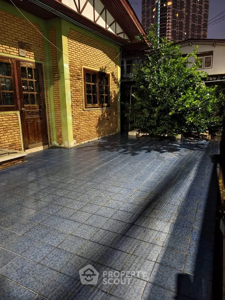 Charming brick house with spacious tiled patio and lush greenery, perfect for outdoor relaxation.