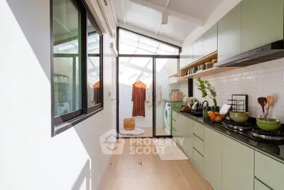 Modern kitchen with sleek green cabinets and natural light, featuring a gas stove and open layout.
