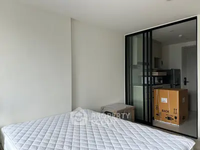 Modern bedroom with sliding glass doors leading to a compact kitchen area, featuring a new appliance box.