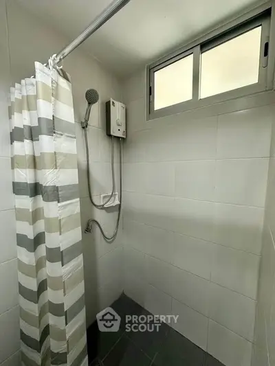 Modern bathroom with shower curtain and window, featuring tiled walls and floor.