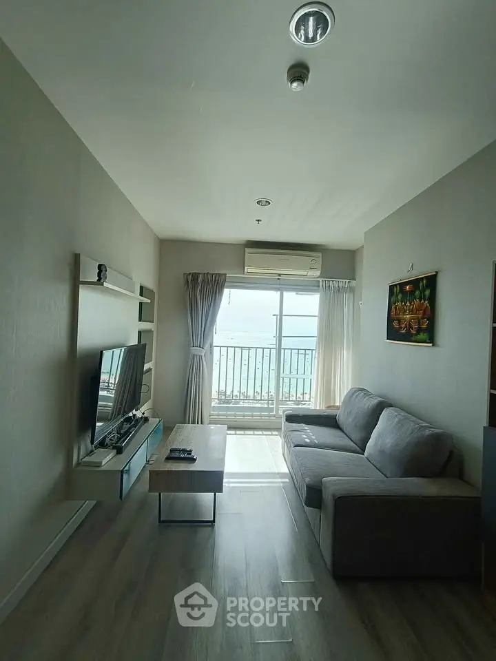 Modern living room with large window and sea view, featuring a cozy sofa and entertainment center.