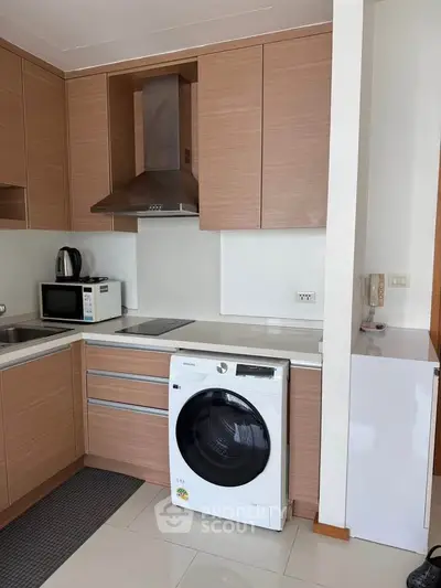 Modern kitchen with sleek wooden cabinets and built-in appliances, featuring a washing machine and microwave.