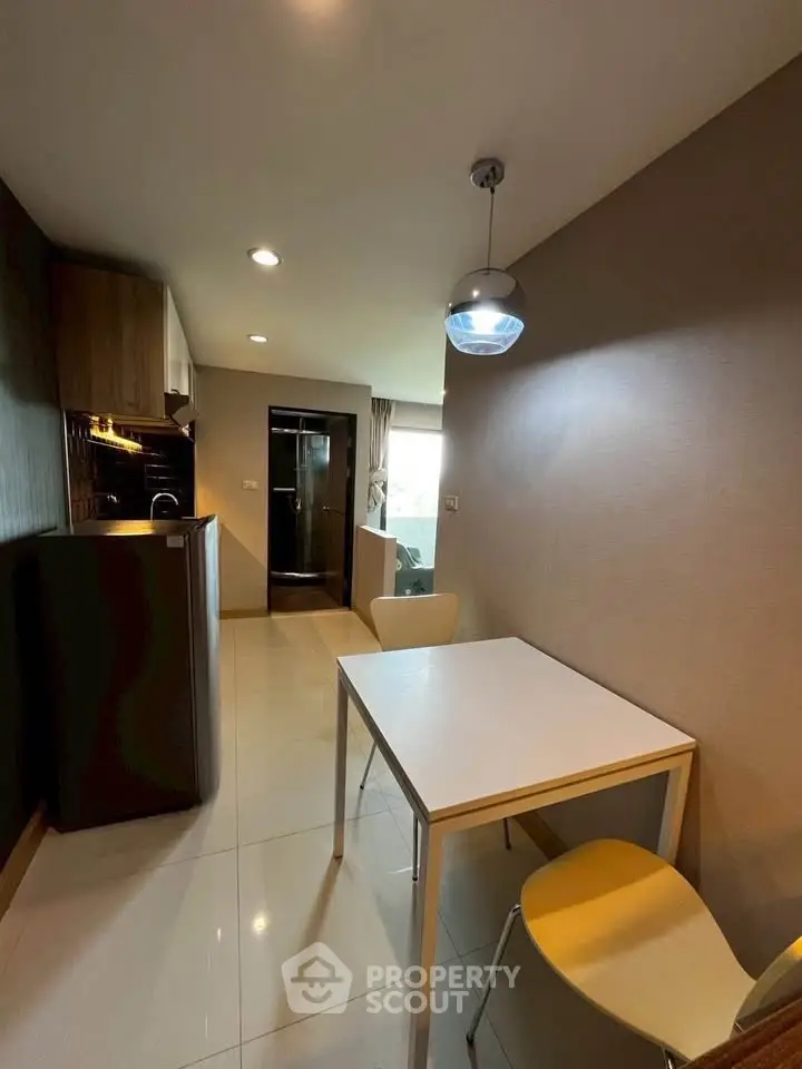 Modern kitchen with dining area in a compact apartment, featuring sleek cabinetry and contemporary lighting.