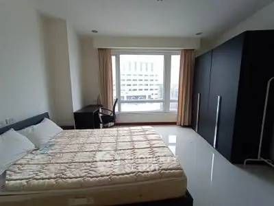 Spacious bedroom with large window and modern furnishings in urban apartment.