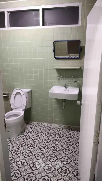 Charming vintage bathroom with green tiles and patterned floor, featuring a classic sink and toilet.
