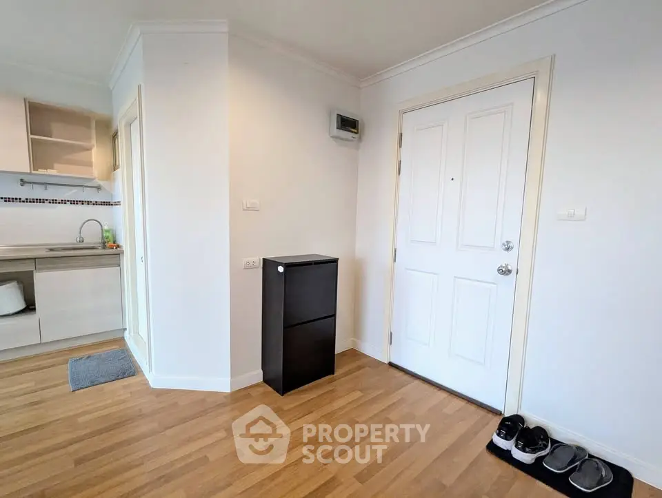Modern apartment entrance with wooden flooring and sleek kitchen view.