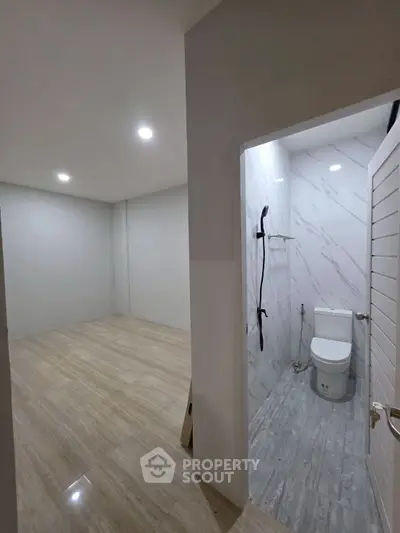 Modern minimalist bathroom with adjacent empty room, featuring sleek fixtures and neutral tones.