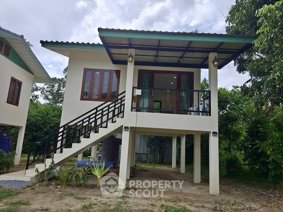 Elevated modern house with lush greenery, featuring a stylish exterior and spacious balcony.