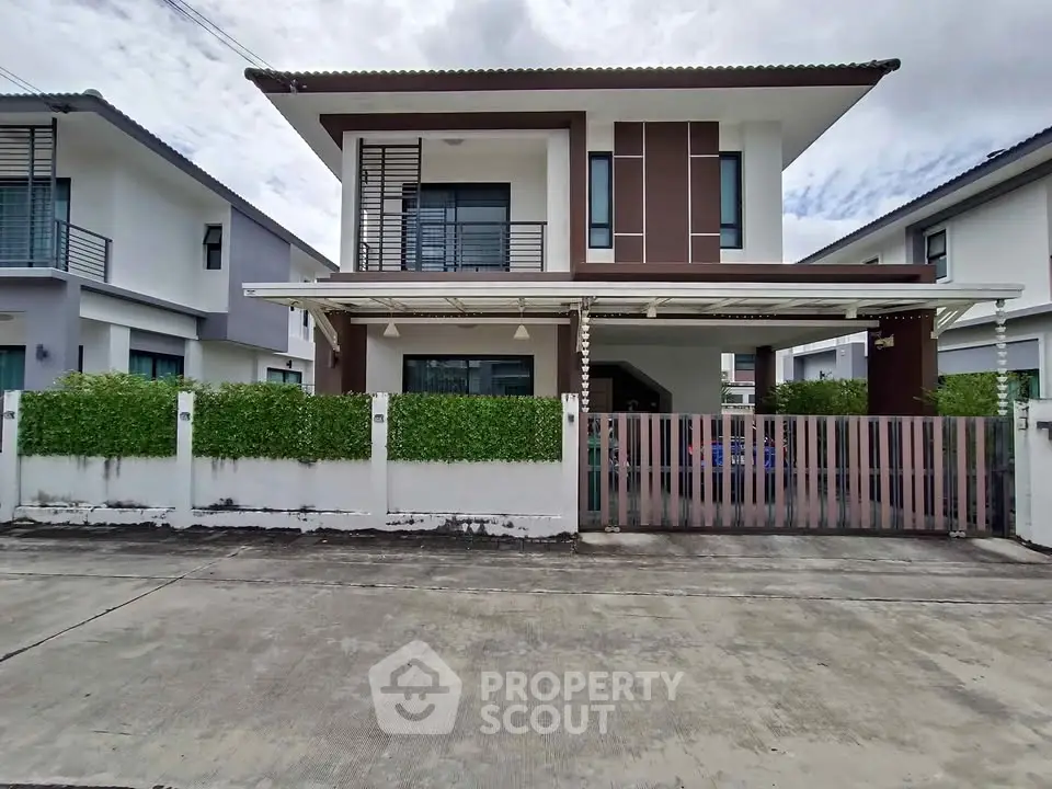 Modern two-story house with gated entrance and lush greenery in a suburban neighborhood.