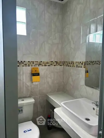 Compact bathroom with modern sink and toilet, featuring stylish tile design and natural light.