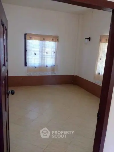 Spacious empty room with tiled floor and natural light from two windows.