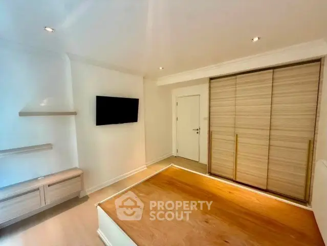 Modern bedroom with built-in wardrobe and wall-mounted TV in a minimalist design.