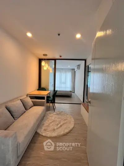Modern open-plan living room with cozy sofa and dining area leading to a bright bedroom.