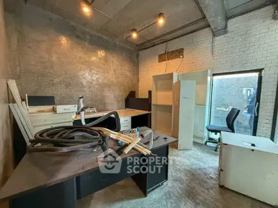 Industrial-style office space with exposed concrete and brick walls, featuring modern lighting and minimalist furniture.