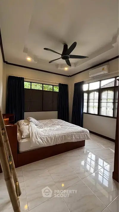 Spacious bedroom with large windows and ceiling fan, perfect for natural light and comfort.