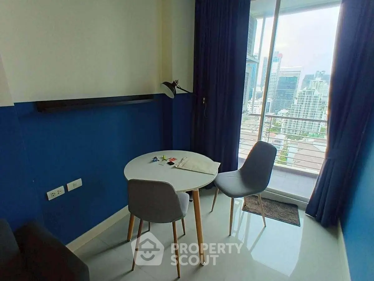 Modern apartment dining area with city view balcony, featuring sleek furniture and vibrant blue accents.