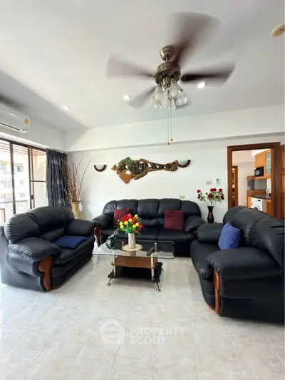 Spacious living room with elegant black leather sofas and ceiling fan, perfect for relaxation.