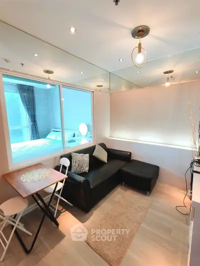 Modern living room with sleek black sofa and dining area, featuring large window and stylish lighting.