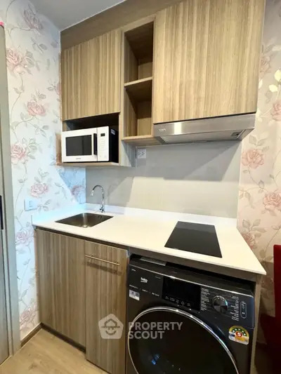 Modern compact kitchen with wooden cabinets, microwave, and washing machine in stylish apartment.