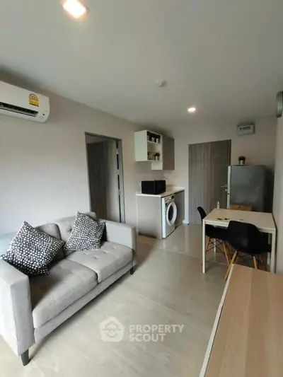 Modern living room with stylish sofa, dining area, and integrated kitchen appliances.