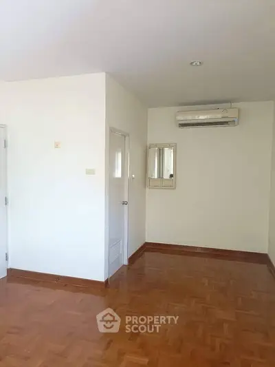 Spacious empty room with wooden flooring and air conditioning, ideal for customization.