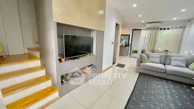 Modern living room with sleek TV setup and cozy seating area, featuring elegant staircase and bright ambiance.