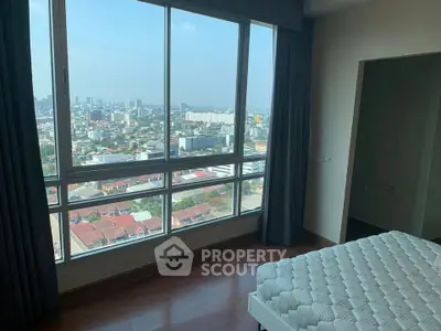 Spacious bedroom with panoramic city view from large windows, featuring modern decor and natural light.