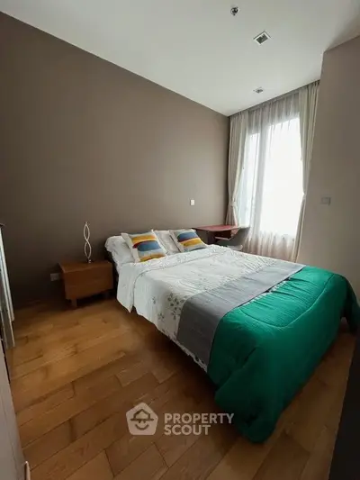 Cozy bedroom with wooden flooring and large window, featuring a comfortable bed and stylish decor.