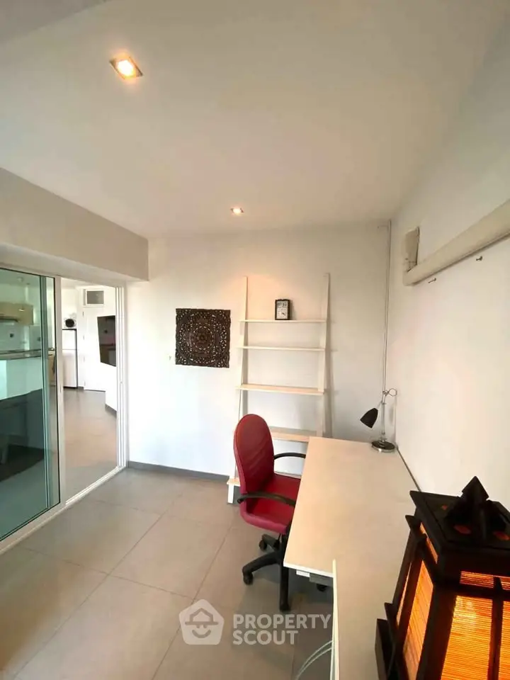 Modern study room with sleek desk and chair, adjacent to a bright kitchen area.