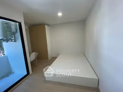 Minimalist bedroom with platform bed and wardrobe, adjacent to a small balcony.