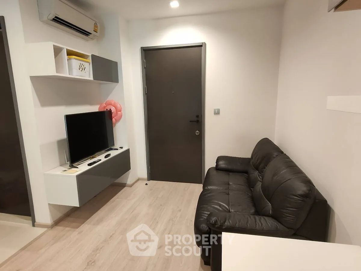 Modern living room with sleek black sofa and wall-mounted TV in cozy apartment.