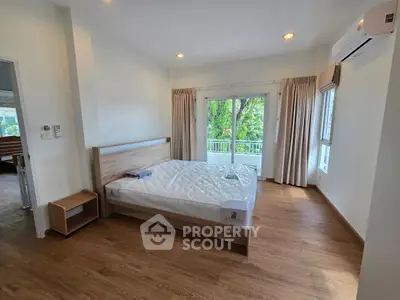 Spacious bedroom with large windows and serene garden view, featuring modern wood flooring and air conditioning.