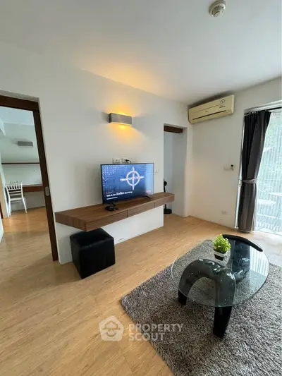 Modern living room with stylish decor, featuring a wall-mounted TV, sleek furniture, and natural light from large windows.