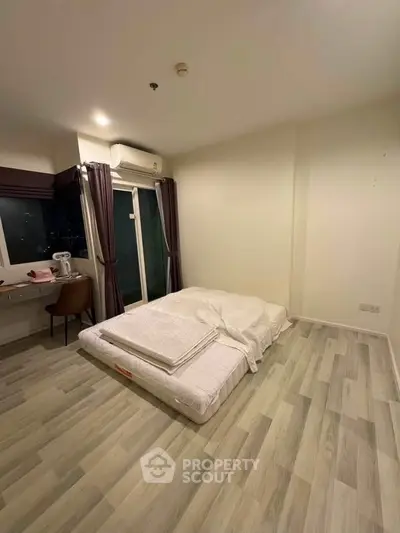 Cozy bedroom with minimalist decor and large window offering city views, perfect for urban living.