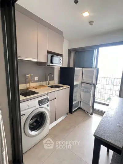 Modern kitchen with washing machine, microwave, and open fridge near balcony view.