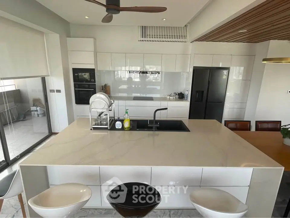 Modern kitchen with sleek island and open layout, featuring black appliances and stylish decor.