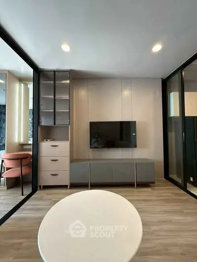 Modern living room with sleek furniture and stylish decor, featuring a mounted TV and elegant lighting.